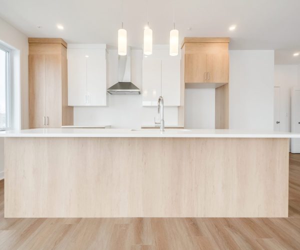Cuisine moderne lumineuse avec grand îlot en bois pâle, comptoir blanc et armoires intégrées sur mesure